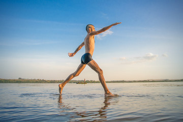 Fototapeta na wymiar Adult man with a mohawk on his head and black shorts running on water against the backdrop of blue sky with clouds