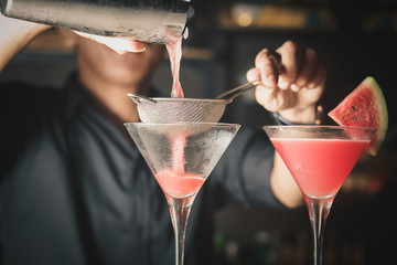 Bartender pouring the cocktail into Martini glass.