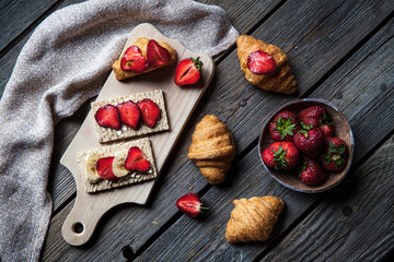 A delicious breakfast of strawberries and bread on wooden background. Fruit, food, sandwiches, cheese. Vintage style.