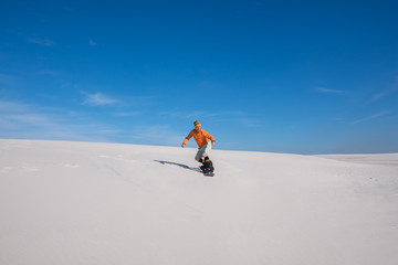 Snowboarder is riding down on the sand dune.