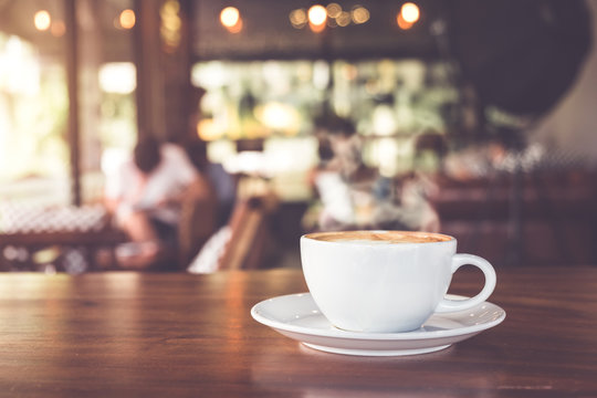 Fototapeta Filiżanka gorąca kawa na stole w kawiarni z ludźmi. efekt kolorystyczny vintage i retro - płytka głębia ostrości
