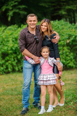 happy family embraces, walks in the park and poses in the camera, the happy daughter smiles and embraces parents