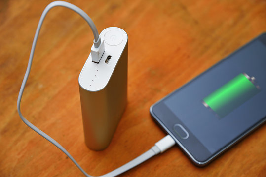 Close-up power bank charging smart phone on wood table.