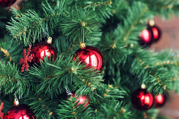 Closeup of red baubles hanging from a decorated Christmas tree.