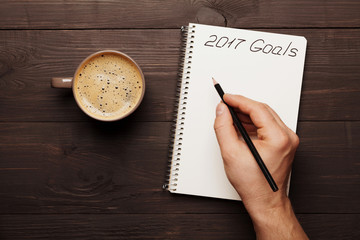 Cup of coffee and male hand writing in notebook goals for 2017. Planning and motivation for the new...
