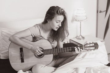 Smiling teen girl playing  on guitar on the bed at home