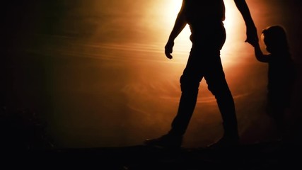 Low section of silhouettes of father and daughter walking against desert-like background in darkly lit studio