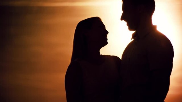 Silhouettes of young man confessing love and proposing to his girlfriend at sunset, then kissing and hugging