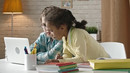 Two little kids doing homework on modern laptop at the desk at home