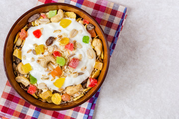 Healthy breakfast with yogurt, muesli and candied fruit in ceramic bowl on stone background