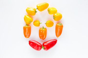 Peperoni rossi gialli e arancioni raffiguranti un viso umano su fondo chiaro