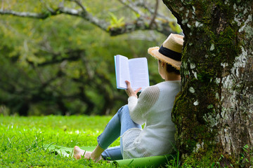 Middle aged woman sitting under a tree reading a book in the park