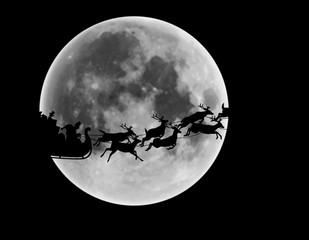 Silhouette of Santa Claus and reindeer riding sleigh in front of full moon in night sky