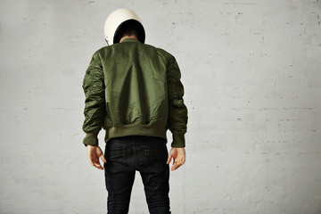 Athletic young model in skinny jeans, green bomber jacket and white motorcycle helmet isolated on...