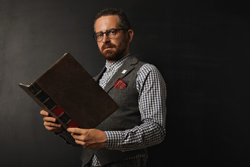 Hip attractive young teacher with a beard wearing tweed suit and checkered shirt holding a leather bound book