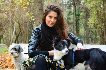 beautiful young woman sitting on a bench with her dogs  in the autumn park 