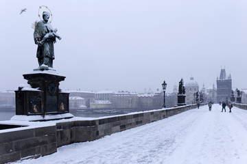 Fototapeta na wymiar Snowy foggy Prague Old Town with Bridge Tower and St. Francis of Assisi Cathedral from Charles Bridge with its baroque Statues, Czech republic