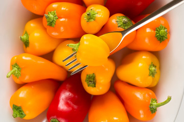 Peperone giallo su forchetta sopra a ciotola bianca con peperoni gialli rossi e arancioni