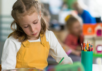 Little girl drawing with pencil in kindergarten.