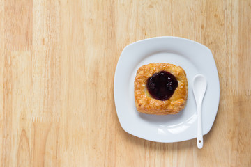 Danish blueberry pie with spoon in white plate on wooden table
