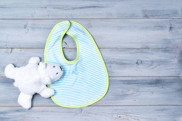 Baby bib and white toy bear on wooden background