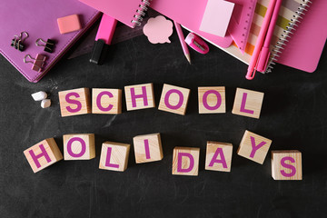 Words SCHOOL HOLIDAYS and stationery set on blackboard background