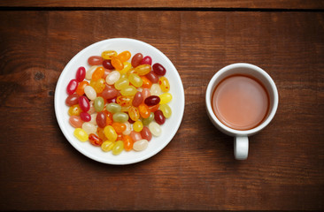 Cup of tea and plate with candies on wooden table