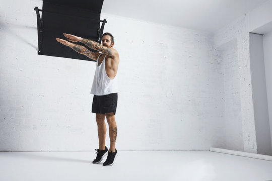 Strong tattooed in white unlabeled tank t-shirt male athlete shows calisthenic moves Squat calf rises