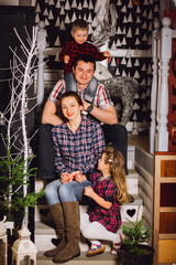Obraz na płótnie Canvas Young family is photographed for Christmas card. Mother, father and little daughter with smile look in camera. They recline on a big bed with bright pillows. Room is decorated with Christmas garlands.