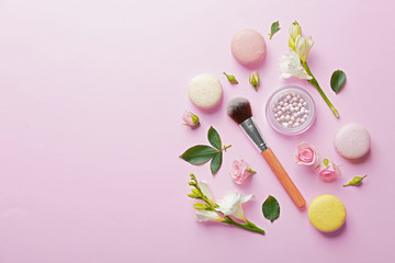 Mineral powder with brush, macaroons and beautiful flowers on pink background