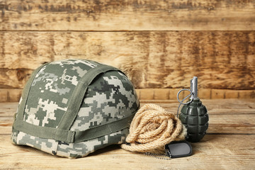 Military helmet, grenade and dog tag on wooden background, close up