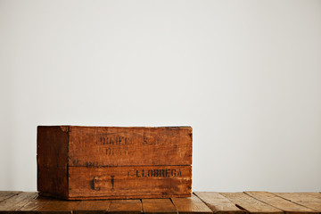 Brown worn rustic box with black letters on a wooden table in a studio with white walls