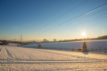 Winterlandschaft mit Oberleitungen für Strom im Gegenlicht bei blauem Himmel