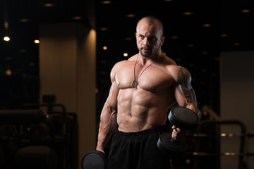 Fototapeta na wymiar Man With Dumbbells Exercising Biceps In Gym