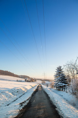 Winterlandschaft mit Oberleitungen f&uuml;r Strom im Gegenlicht bei blauem Himmel