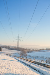 Winterlandschaft mit Oberleitungen für Strom im Gegenlicht bei blauem Himmel