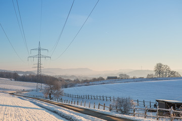 Fototapeta premium Winterlandschaft mit Oberleitungen für Strom im Gegenlicht bei blauem Himmel