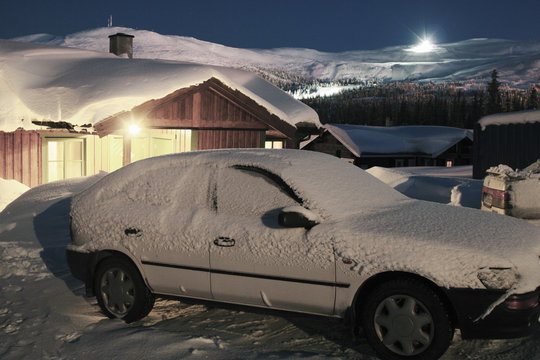 Snow covered car parked outside house at dusk