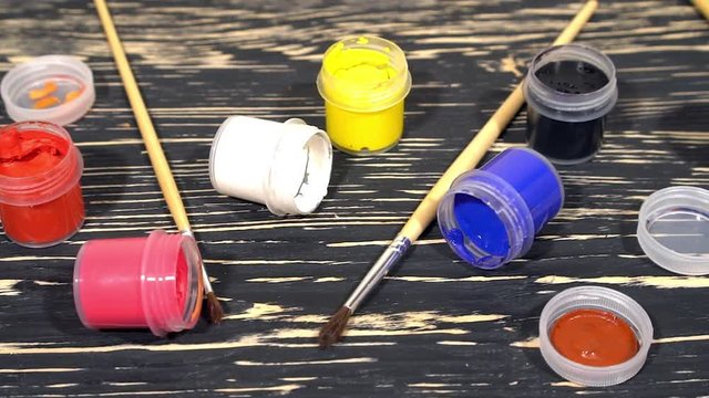 A lot of varicolored paint gouache jars with brushes on wooden background