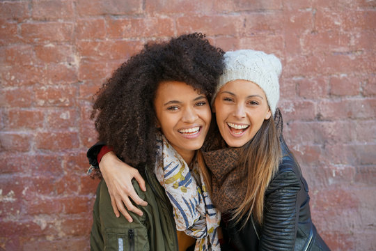 Portrait Of Trendy Girls Hugging In Front Of Brick Wall