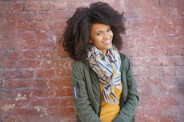 Trendy mixed-raced girl standing by brick wall