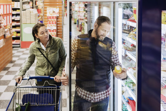 Couple buying groceries while standing by refrigerator in supermarket