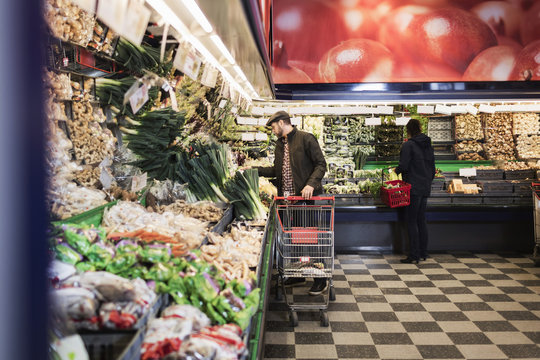 Man buying vegetables while holding shopping cart in supermarket