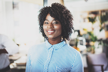 Fototapeta premium Portrait of pretty african american business woman with afro looking and smiling at the camera.Interior on background in modern office. Horizontal,blurred.