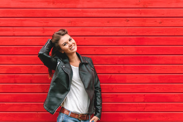 Portrait of a beautiful young woman in a leather jacket on the background of a red wooden wall