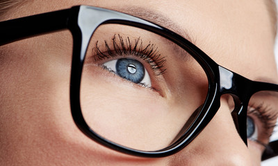Close-up of female blue eye wearing spectacles with black frame. Concept of human vision, sight examination and care.    - 126124561