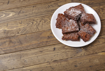 A plate full of freshly baked chocolate fudge brownies on a rustic wooden table background with blank space at side