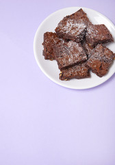 A plate full of freshly baked chocolate fudge brownies on a pastel purple background with empty space below