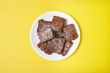 Aerial view of a plate full of freshly baked chocolate fudge brownies on a bright yellow background