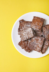 A plate full of freshly baked chocolate fudge brownies on a bright yellow background